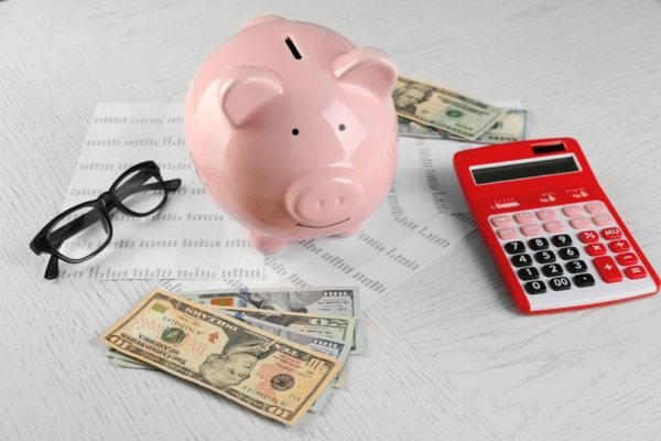 glasses, dollar bills, calculator, piggy bank and list of expenses depicting savings