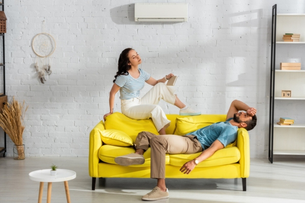 couple feeling warm and exhausted in front of AC due to insufficient cooling