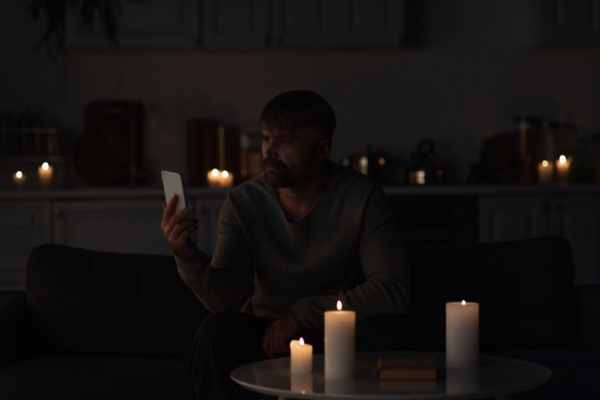 man looking at mobile phone surrounded by candles due to power surge
