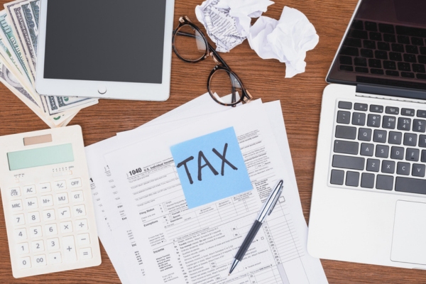 Top view of tax forms, digital devices and tax word handwritten on a blue card