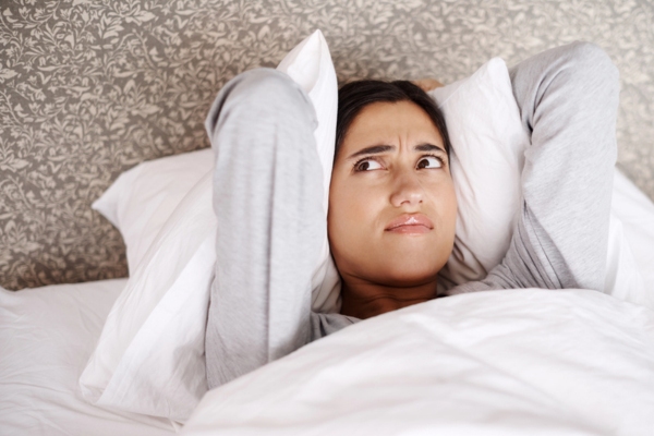 young lady covering ears with pillow on the bed due to noise coming from window air conditioner