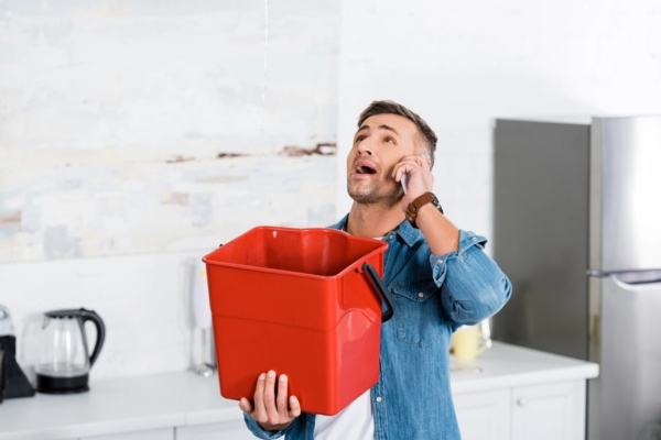 Man talking on smartphone while holding plastic bucket up due to water leak from air conditioner