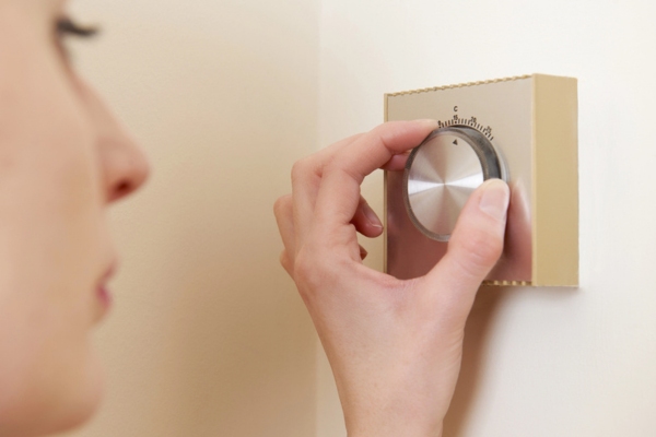 woman adjusting central heating thermostat