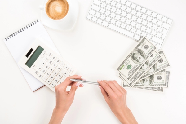 woman holding a pen beside a calculator and dollar bills depicting Driving Up Winter Costs