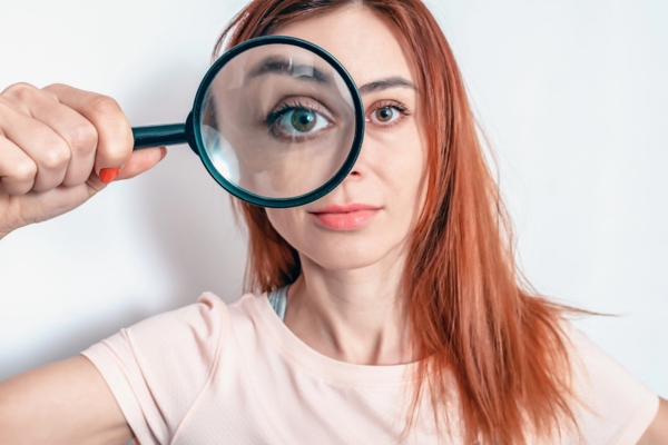 woman holding a magnifying glass on her right eye depicting identifying signs of leaking HVAC ductwork